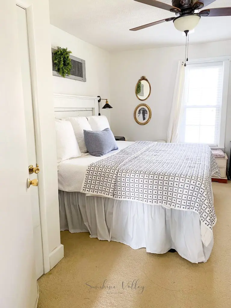 farmhouse bedroom with DIY headboard blue and white quilt and thrift store wall art